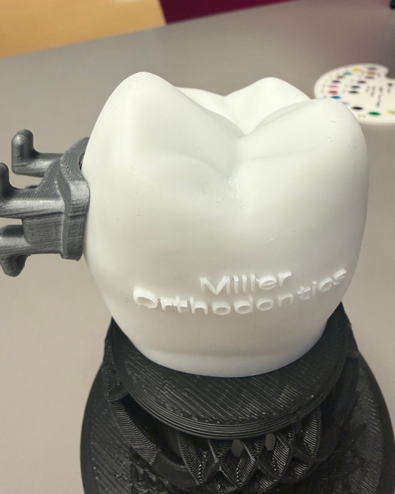 A large 3D-printed model of a molar with a custom bracket attached and Miller Orthodontics printed on its side