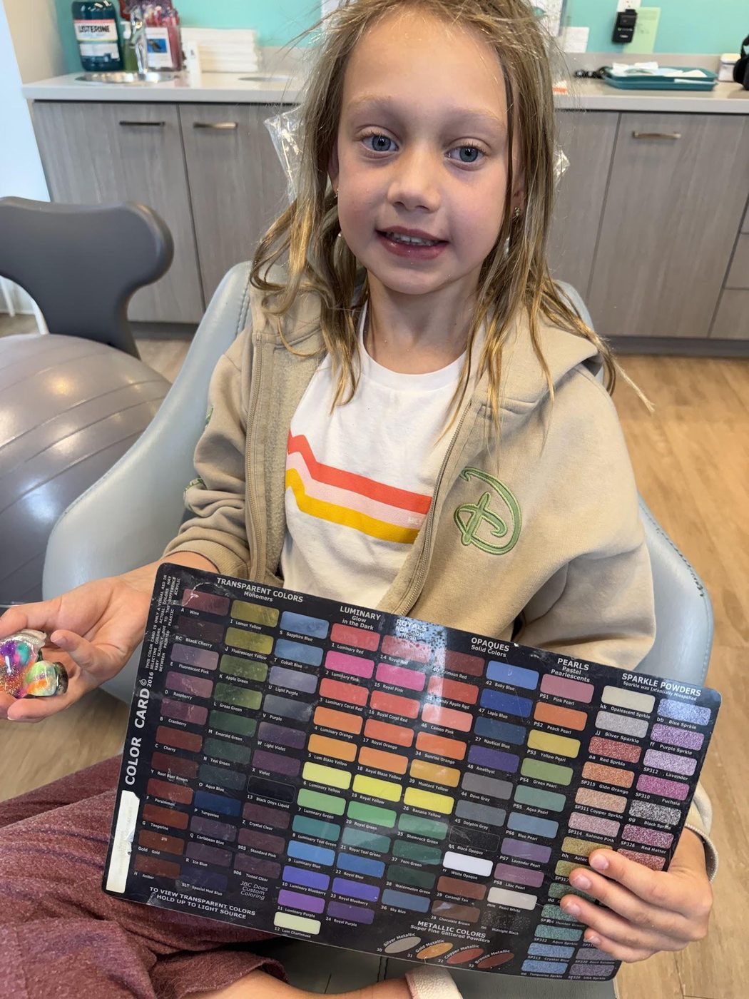 A young patient in the treatment chair holding a color card to pick the colors for her braces